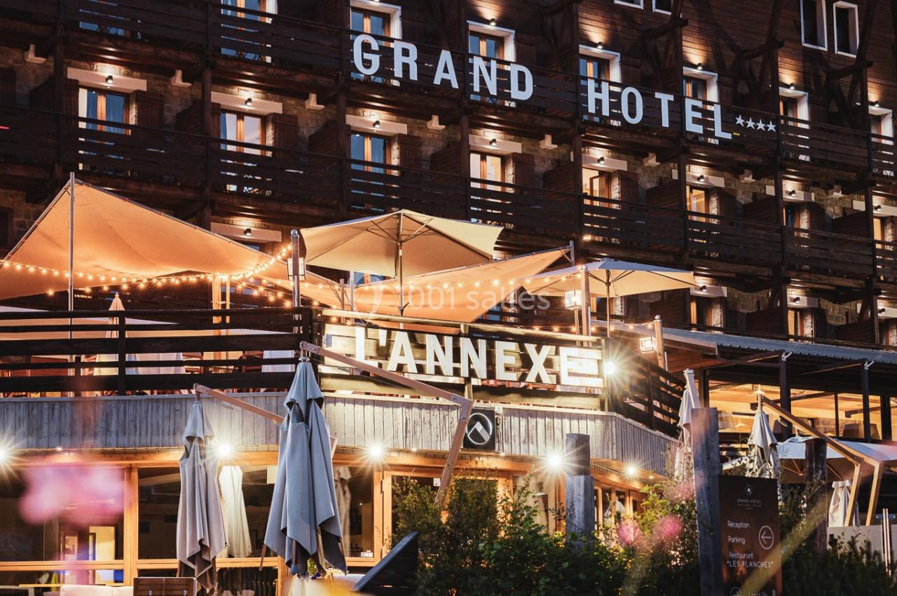Façade éclairée d'un hôtel en bois avec terrasses illuminées, vue de nuit et fleurs au premier plan.