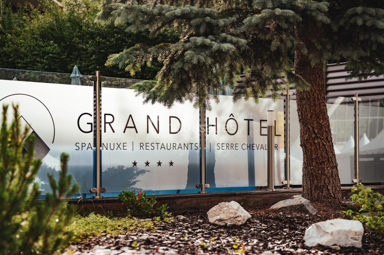 Panneau indiquant ’Grand Hôtel’ avec mentions de spa, restaurants et étoiles, entouré de végétation et d'arbres.