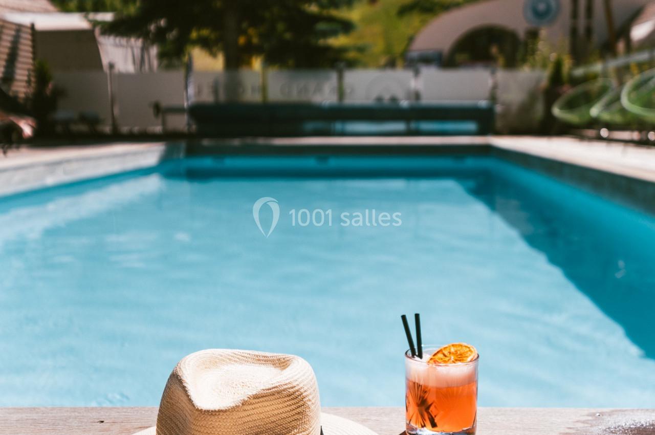 Chapeau, lunettes de soleil et cocktail posés sur une terrasse en bois au bord d'une piscine extérieure, avec paysage en…
