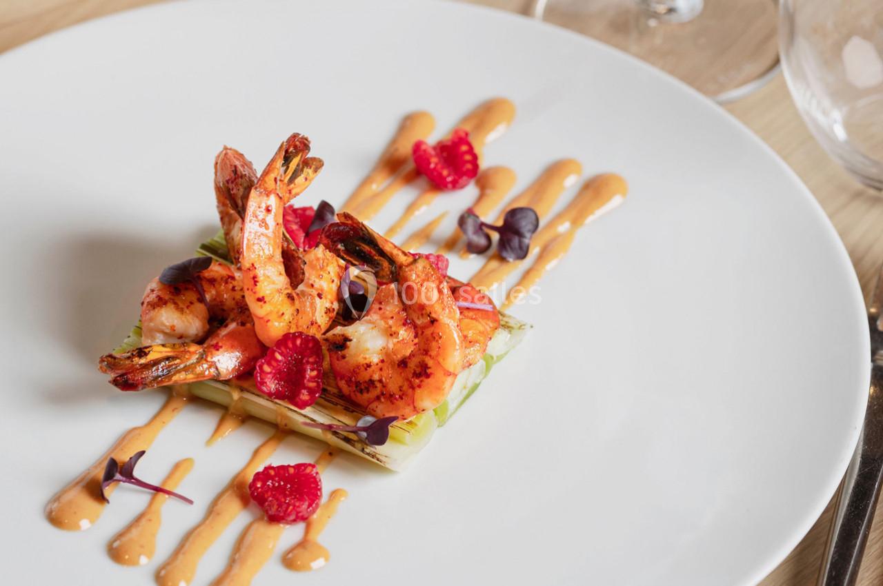 Assiette de crevettes grillées sur lit de légumes, décorée de framboises, pousses et sauce disposée en traits.