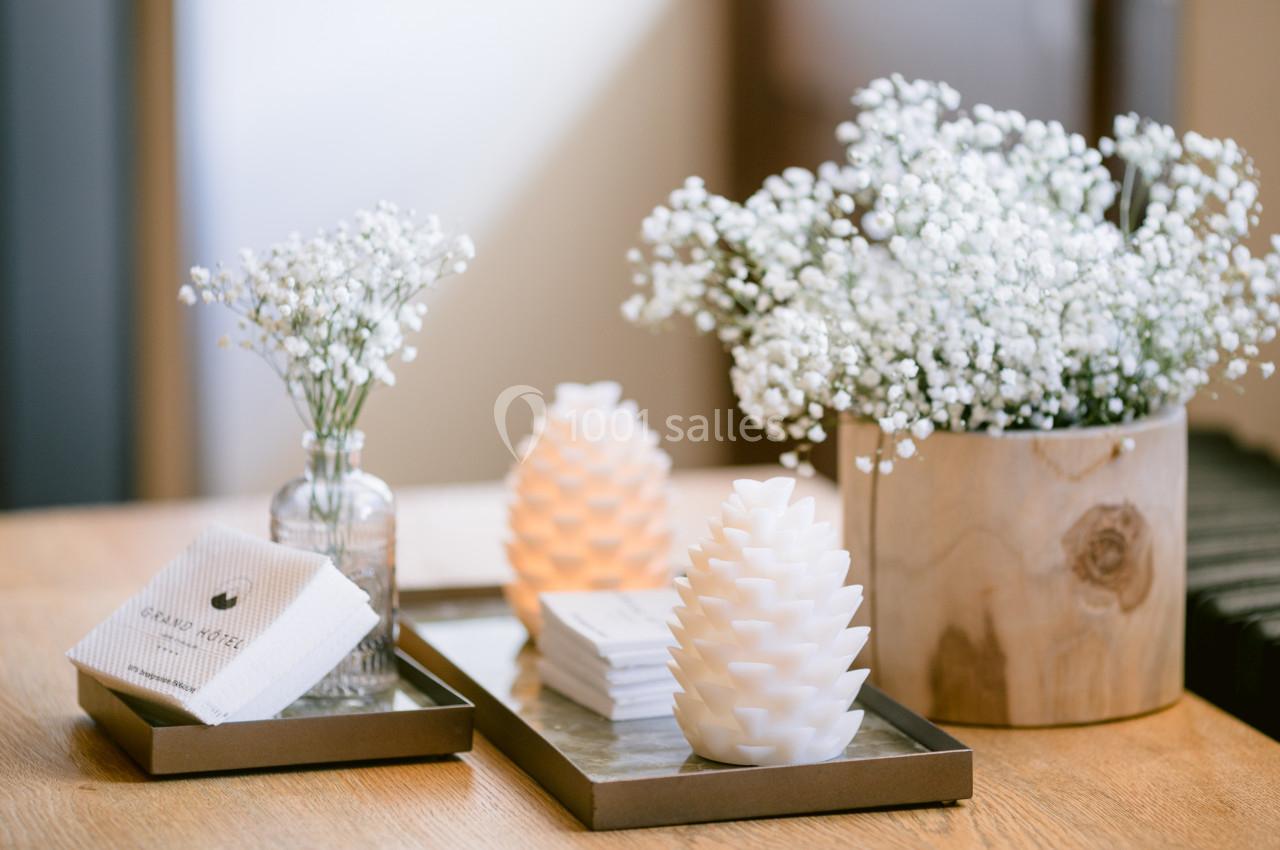 Bougies en forme de pommes de pin et bouquets de gypsophile disposés sur un plateau en bois clair.