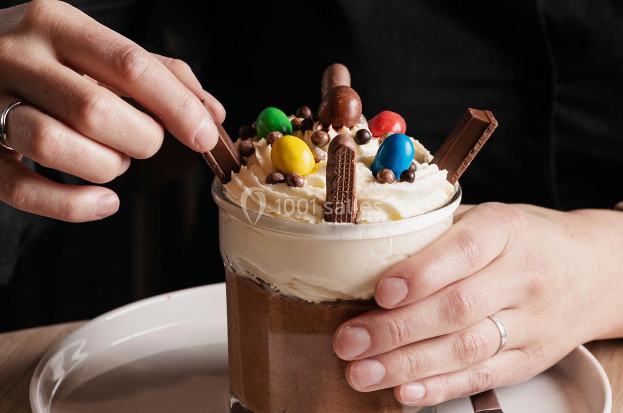 Personne décorant un dessert au chocolat garni de crème fouettée, bonbons colorés et morceaux de chocolat.