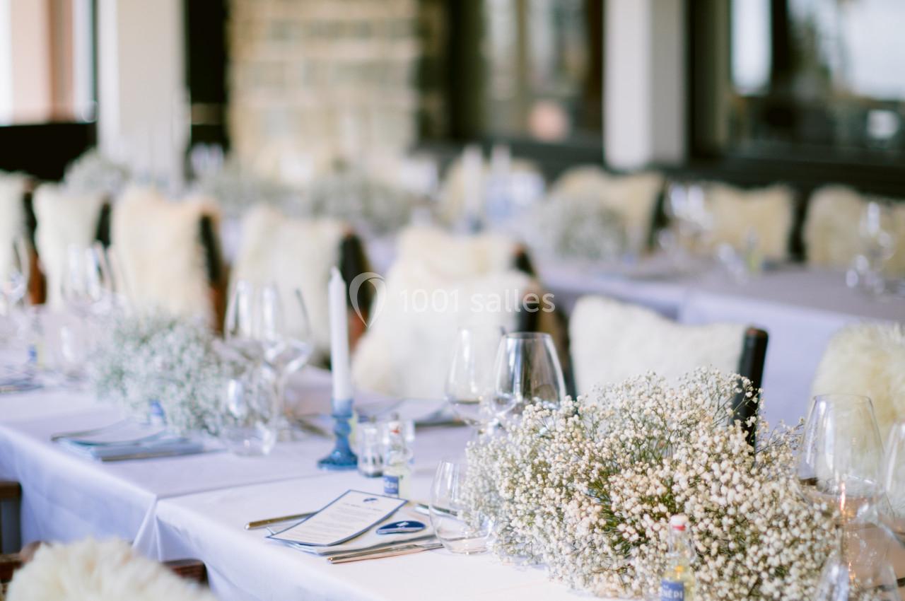 Table dressée avec nappes blanches, chaises couvertes de fourrure, décorations florales et bougies dans un intérieur élégant.