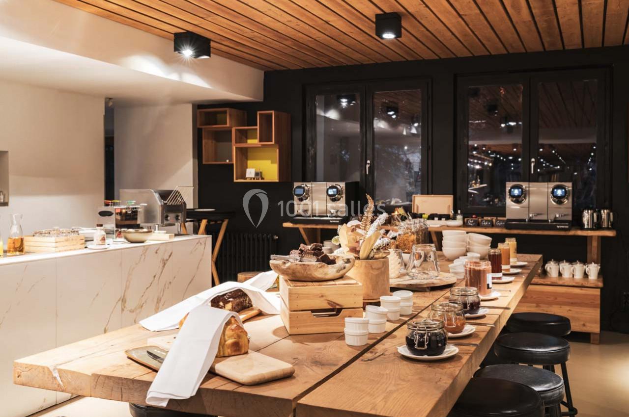 Buffet de petit-déjeuner avec pains, confitures, céréales et boissons, présenté sur une table en bois dans une salle…