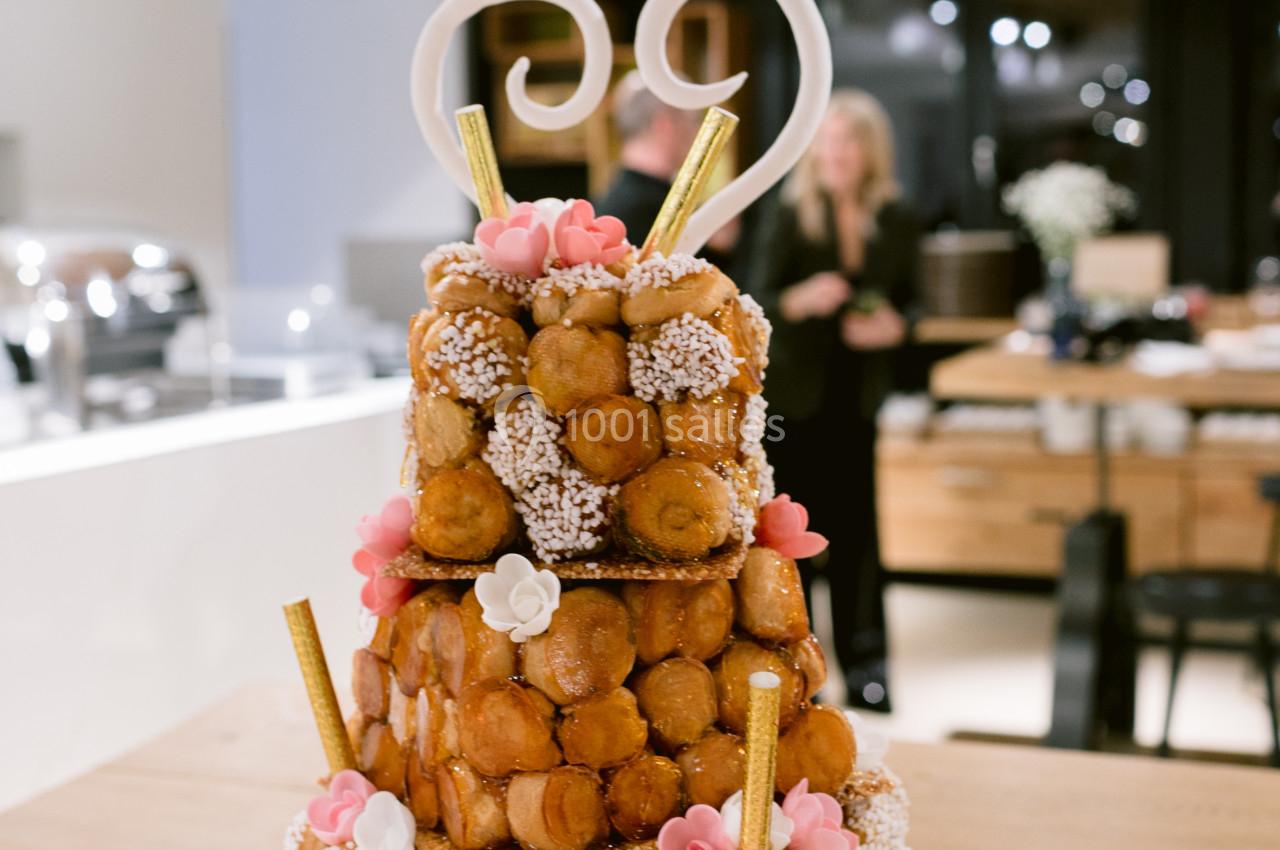 Pièce montée en choux décorée de fleurs en sucre, spirales en chocolat et macarons, posée sur une table en bois.