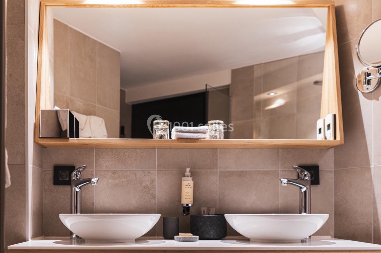 Deux lavabos blancs avec robinets modernes devant un grand miroir encadré en bois dans une salle de bain lumineuse.