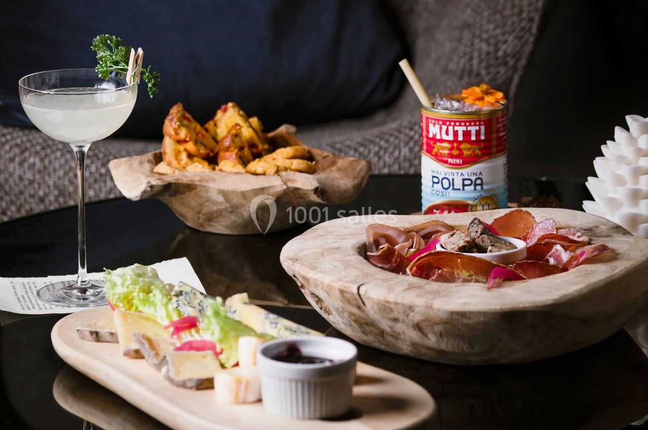 Plateau de charcuterie, fromage et pain, cocktail, pommes de terre épicées et conserve de tomates sur une table basse.