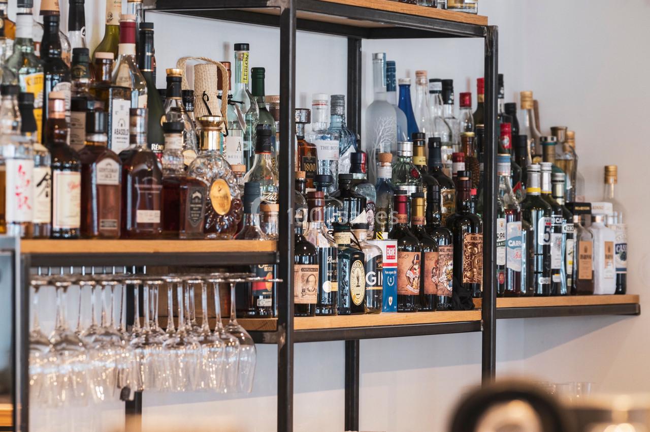 Étagères remplies de bouteilles d'alcool variées dans un bar, avec des verres suspendus en dessous.