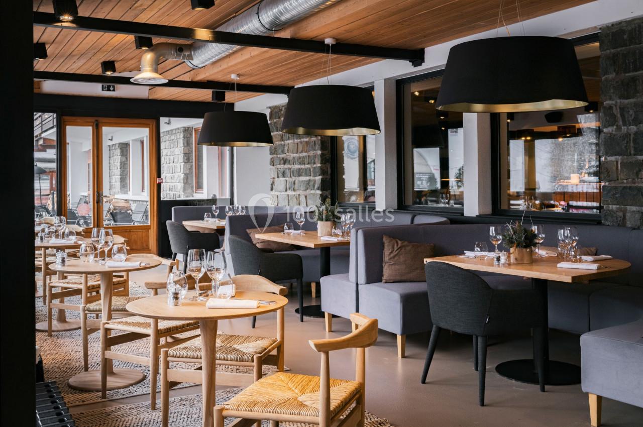 Salle de restaurant moderne avec tables en bois, chaises en osier et luminaires noirs suspendus.