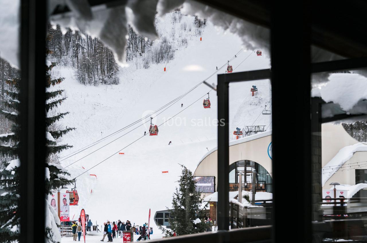 Vue d'une station de ski avec des télécabines, des skieurs sur une piste enneigée et des bâtiments au premier plan.