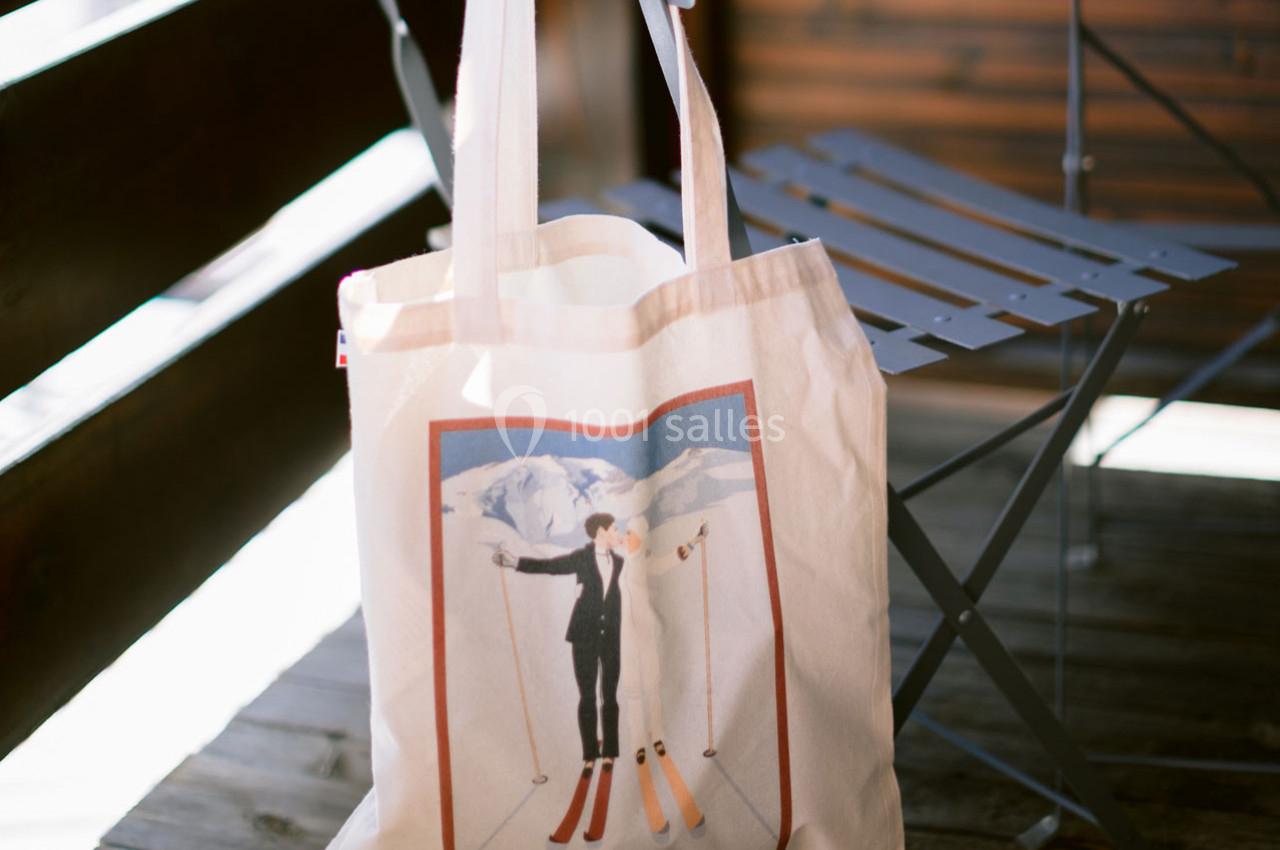 Sac en toile posé sur une chaise pliante, illustré d'une scène de ski avec deux skieurs devant un paysage montagneux.