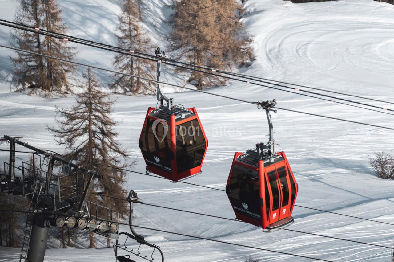 Deux cabines rouges de télécabine suspendues au-dessus d'un paysage enneigé avec des arbres en arrière-plan.