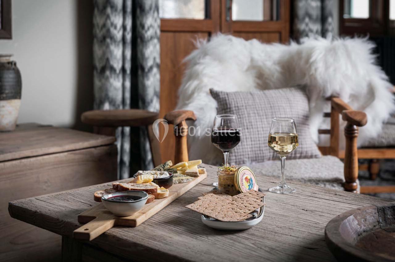 Plateau de fromages et charcuteries avec deux verres de vin sur une table en bois dans un salon cosy.