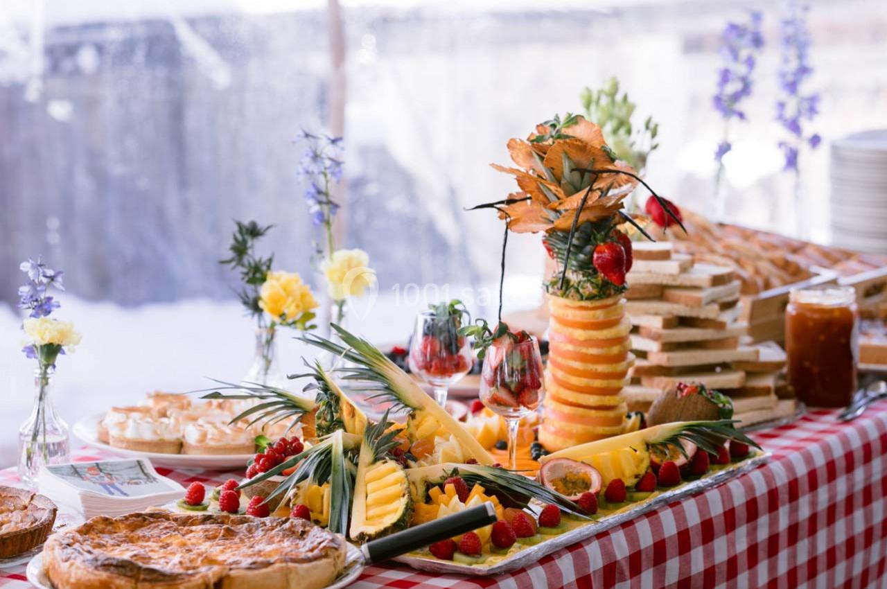 Buffet avec fruits frais, pâtisseries, pain et confitures sur une nappe à carreaux rouges et blancs.