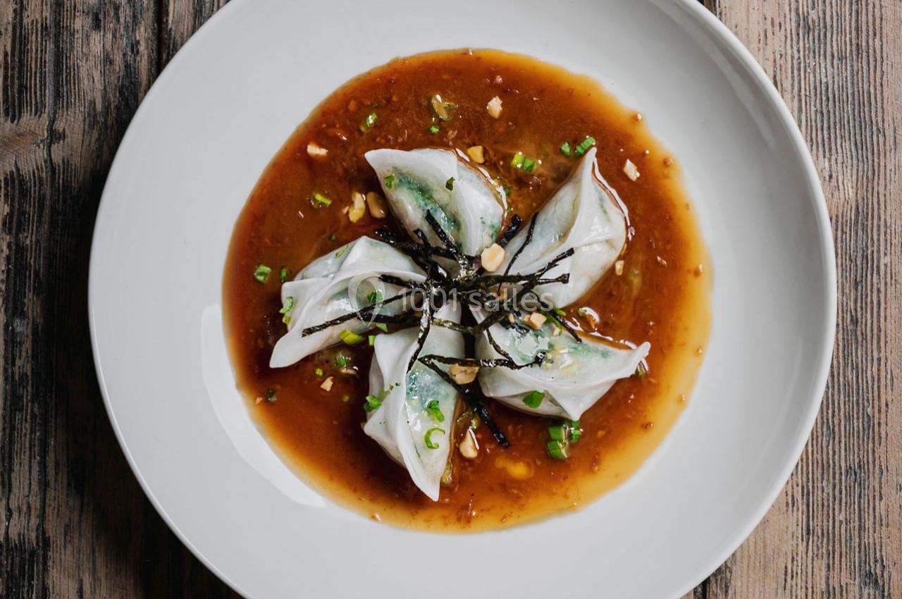 Assiette de raviolis vapeur garnis de légumes, servis avec une sauce brune et décorés d'algues et de ciboulette.
