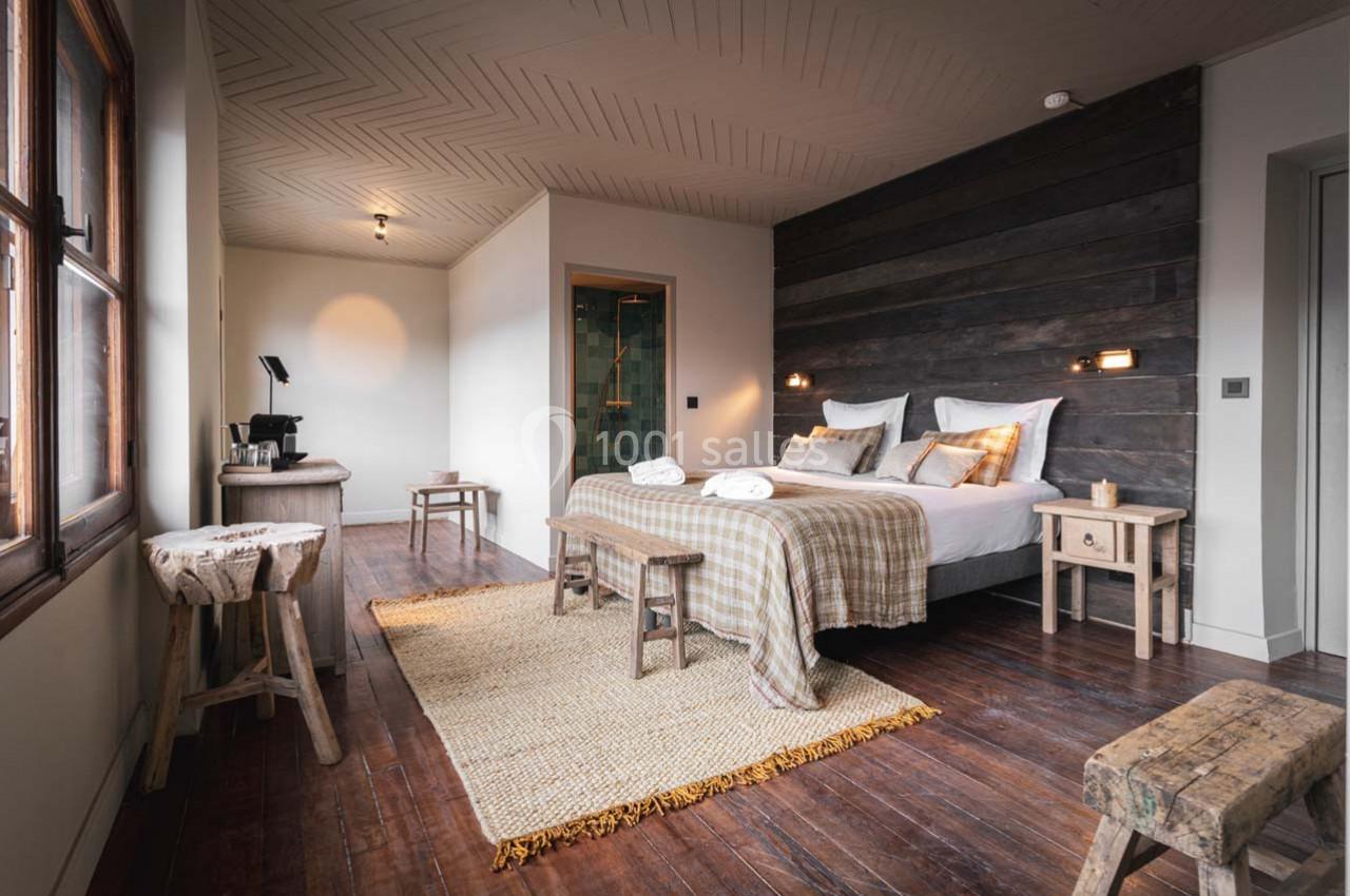 Chambre lumineuse avec lit double, mobilier en bois rustique, sol en parquet et salle de bain attenante.