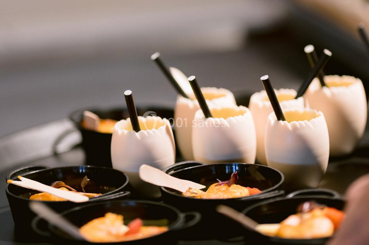 Des verrines en coquilles d'œufs et des mini-casseroles noires contenant des préparations culinaires sur un plateau.