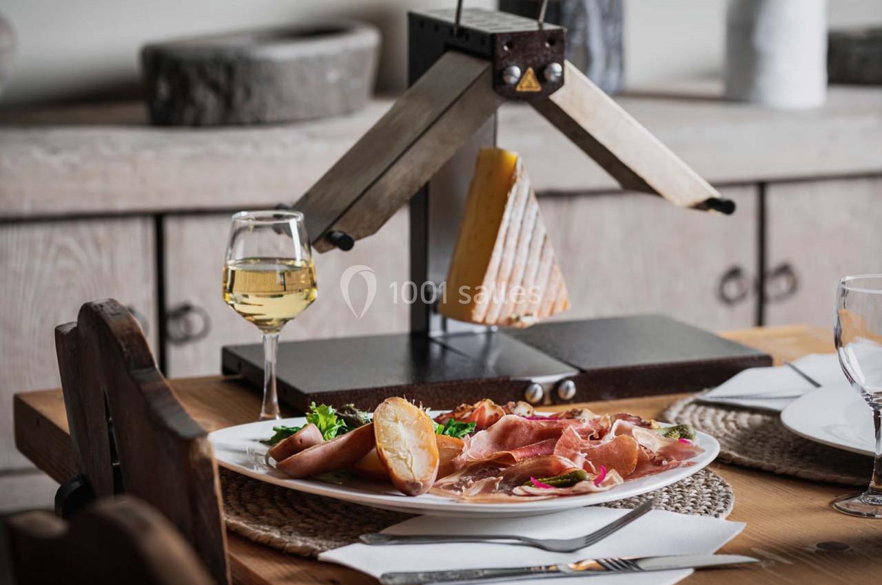 Assiette de raclette avec charcuterie, pommes de terre et salade, servie à côté d'un appareil à raclette et d'un verre de…
