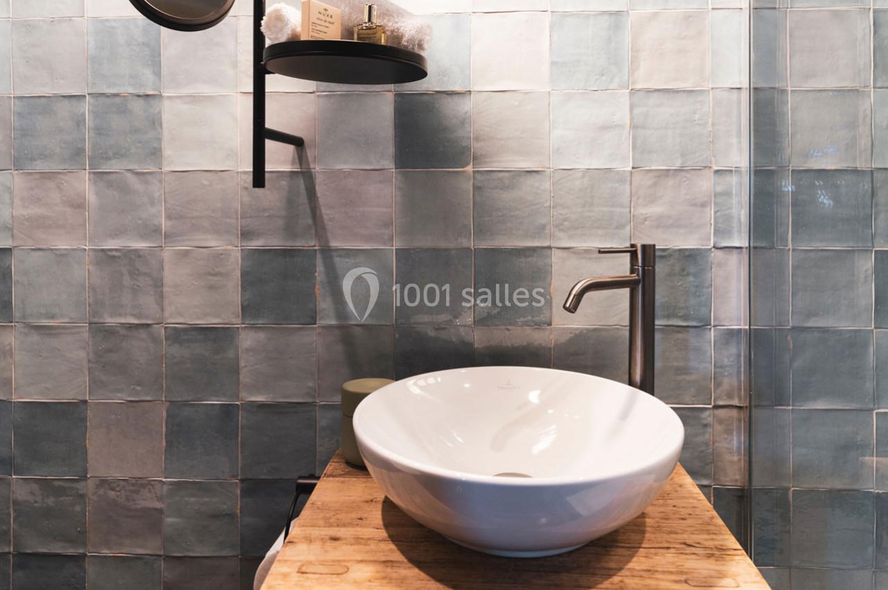 Lavabo blanc posé sur un meuble en bois, avec un robinet métallique et un mur de carreaux bleus en arrière-plan.