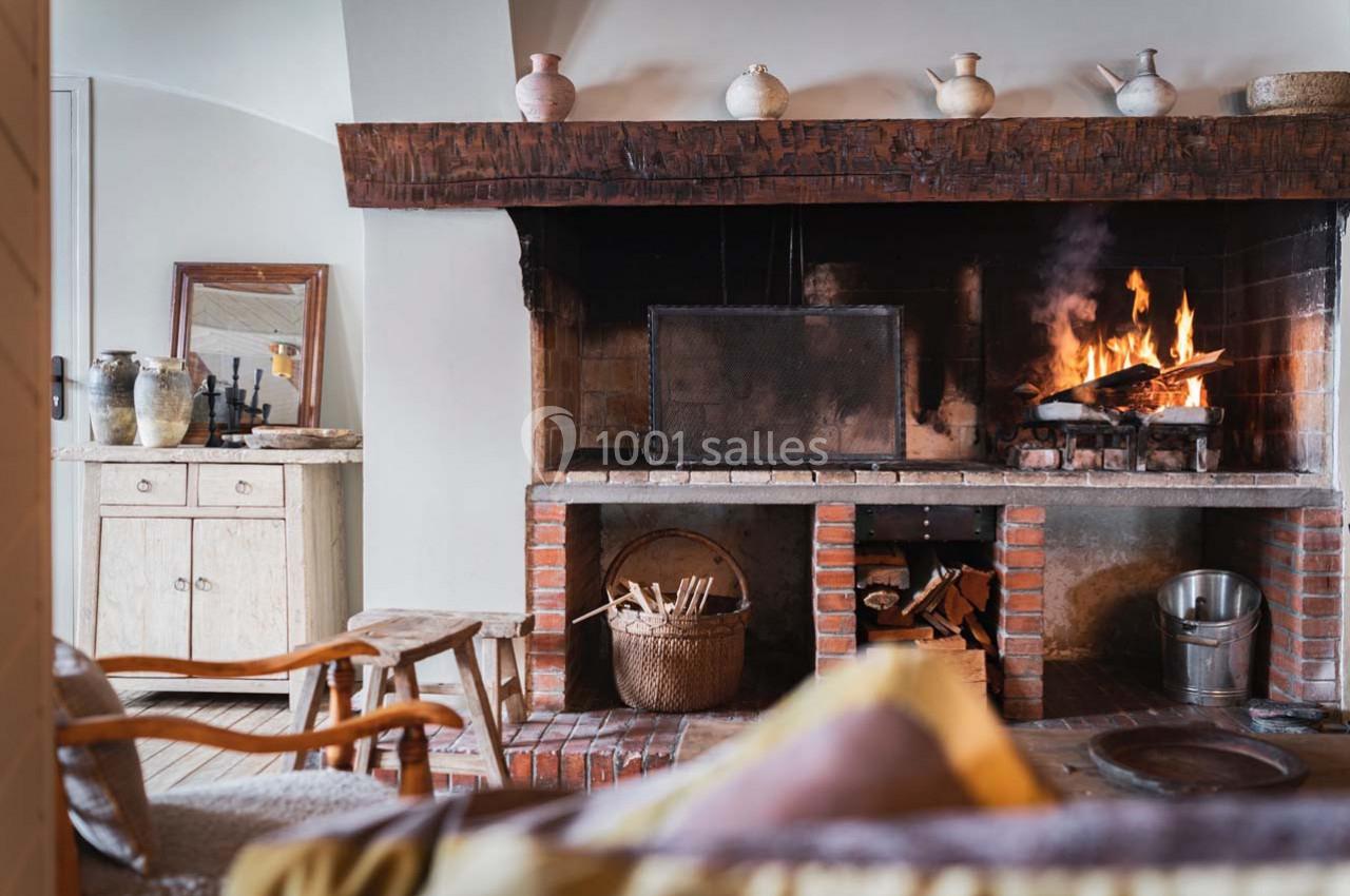 Cheminée en pierre avec feu de bois allumé, entourée de pots décoratifs et mobilier rustique en bois.