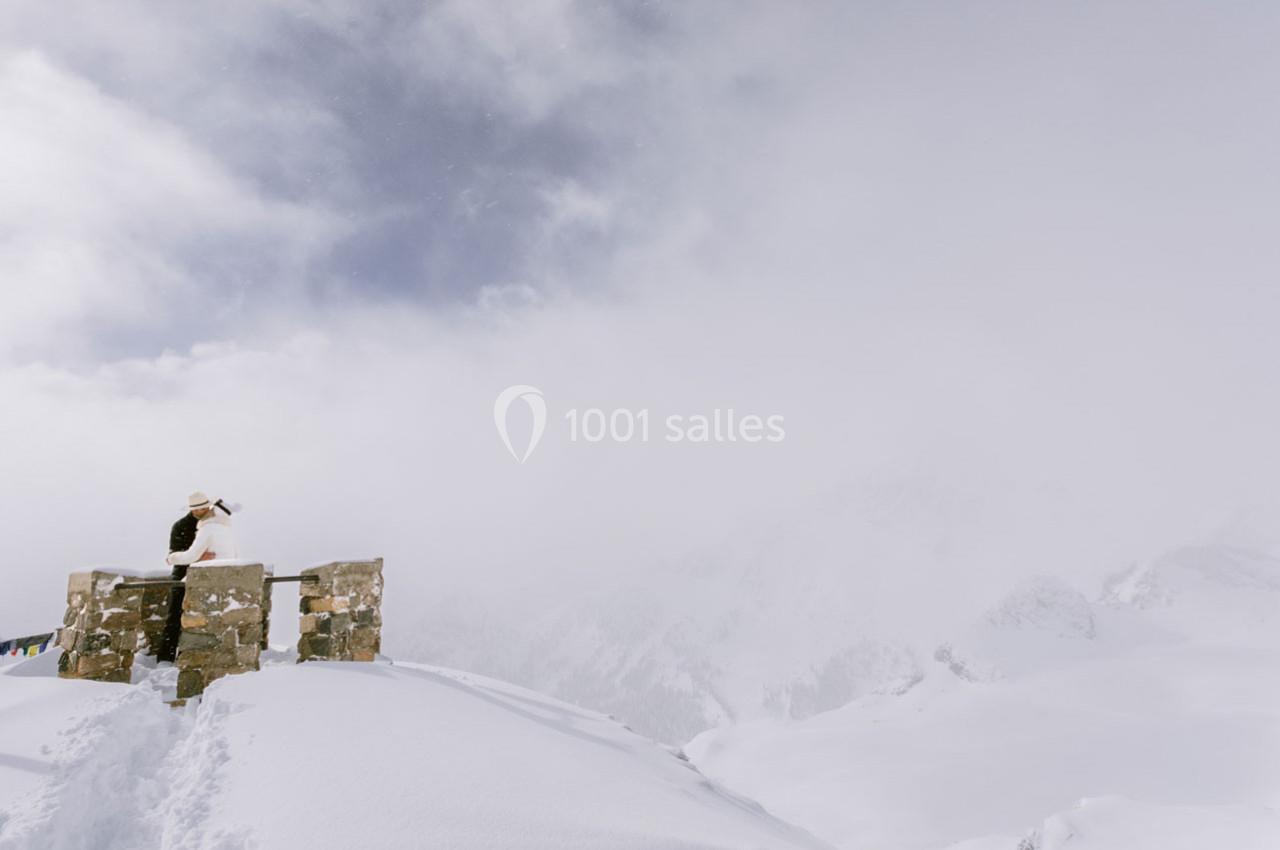 Une personne debout sur une plateforme en pierre observe un paysage enneigé sous un ciel nuageux.