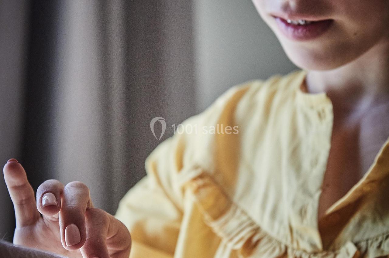 Une jeune femme en chemisier jaune attache un bracelet au poignet d'une autre personne dans un intérieur lumineux.