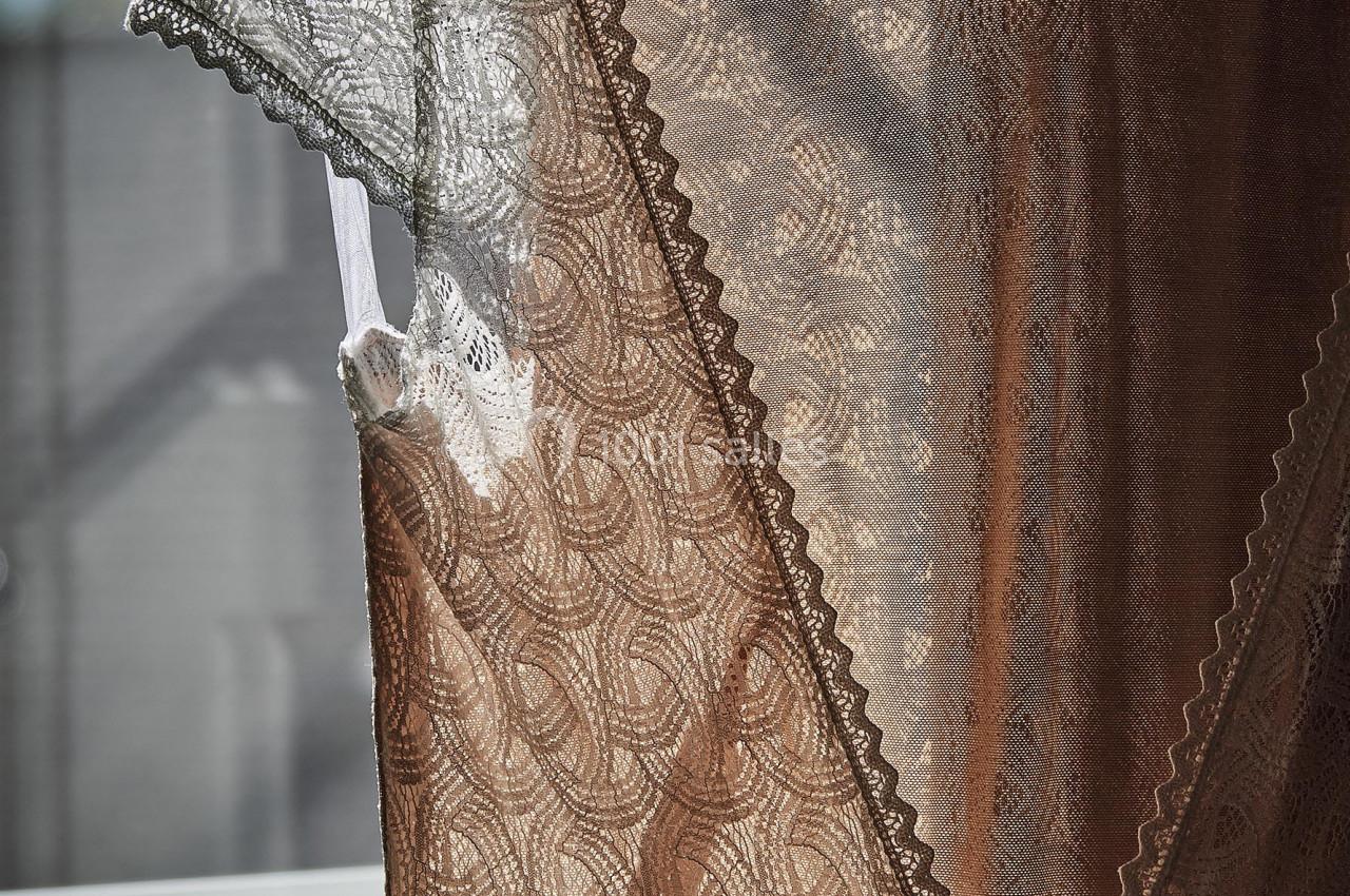 Robe en dentelle beige suspendue à un cintre, éclairée par la lumière naturelle d'une fenêtre.