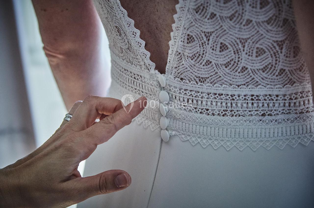Main ajustant les boutons d'une robe de mariée en dentelle blanche vue de dos.