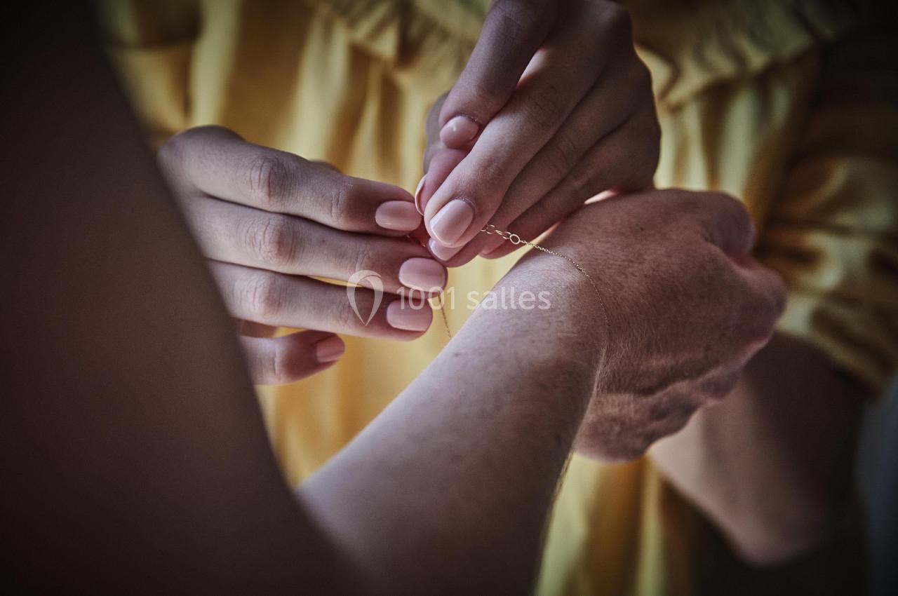 Une personne attache un bracelet fin au poignet d'une autre, en arrière-plan une tenue jaune.