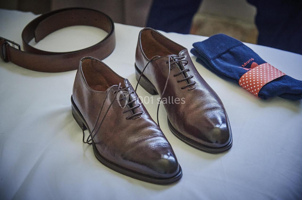 Chaussures en cuir marron avec lacets, ceinture assortie et paire de chaussettes bleues posées sur une table blanche.