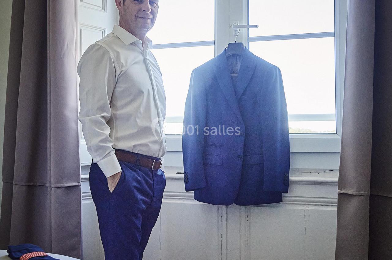 Un homme debout près d'une fenêtre lumineuse, avec une veste de costume suspendue devant celle-ci.