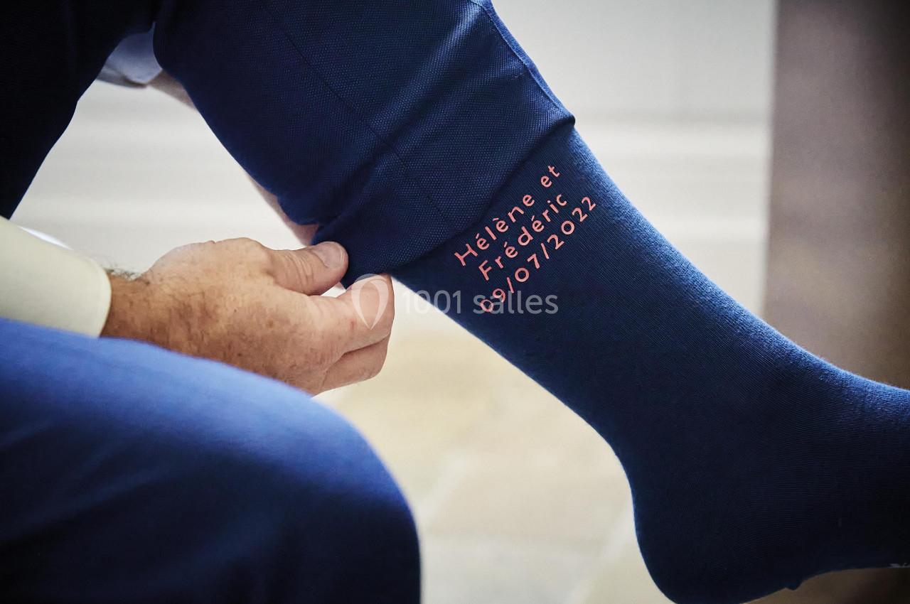 Homme ajustant une chaussette bleue personnalisée avec les prénoms ’Hélène et Frédéric’ et une date inscrite.