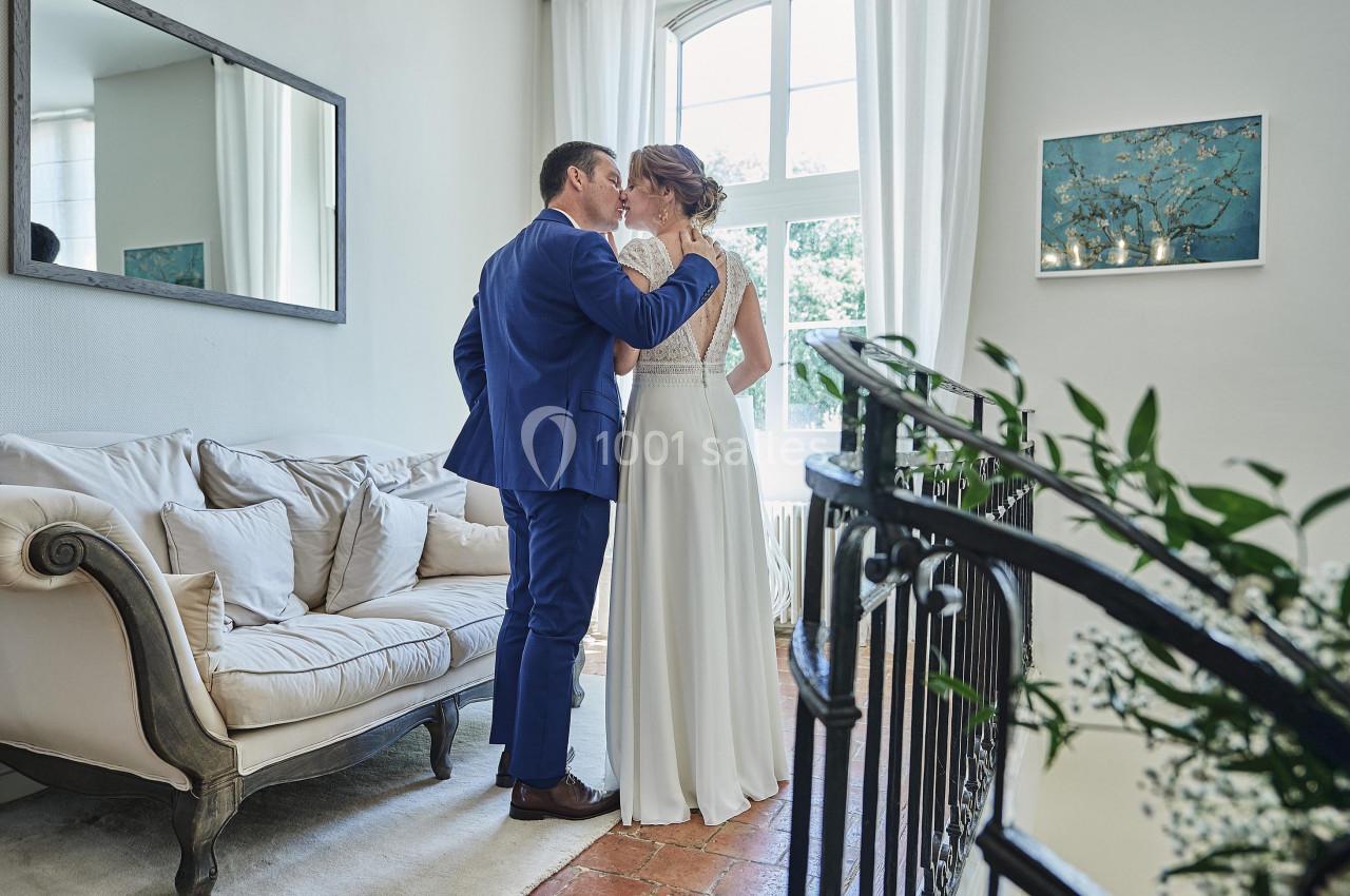 Un couple en tenue de mariage s'embrasse dans un salon lumineux près d'une fenêtre.
