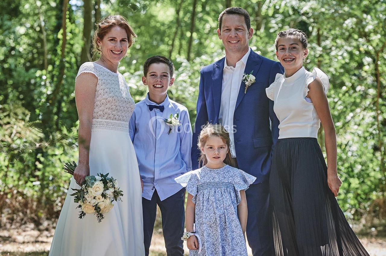 Une famille posant dans un cadre naturel, avec un couple en tenue de mariage entouré de trois enfants.