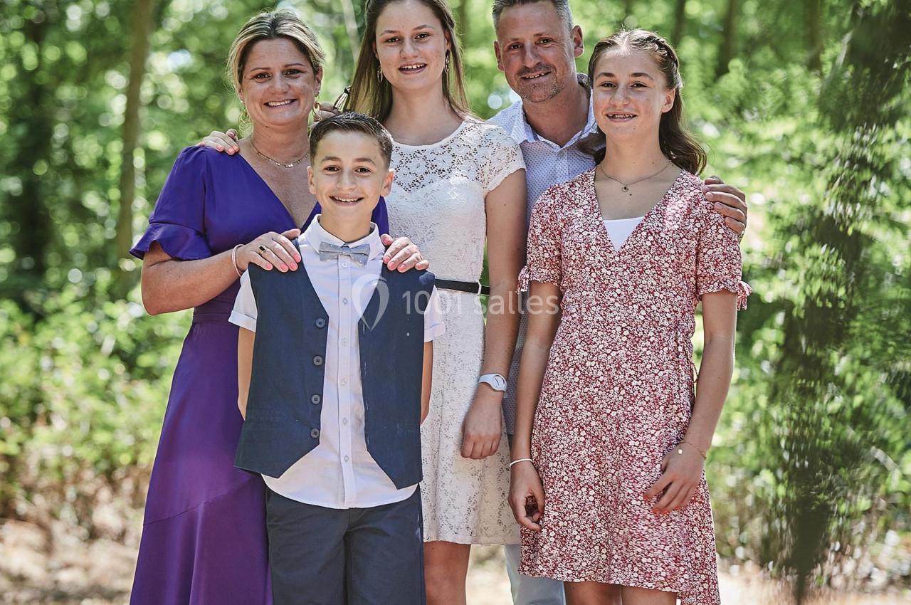 Une famille de cinq personnes posant ensemble dans un environnement boisé et ensoleillé.