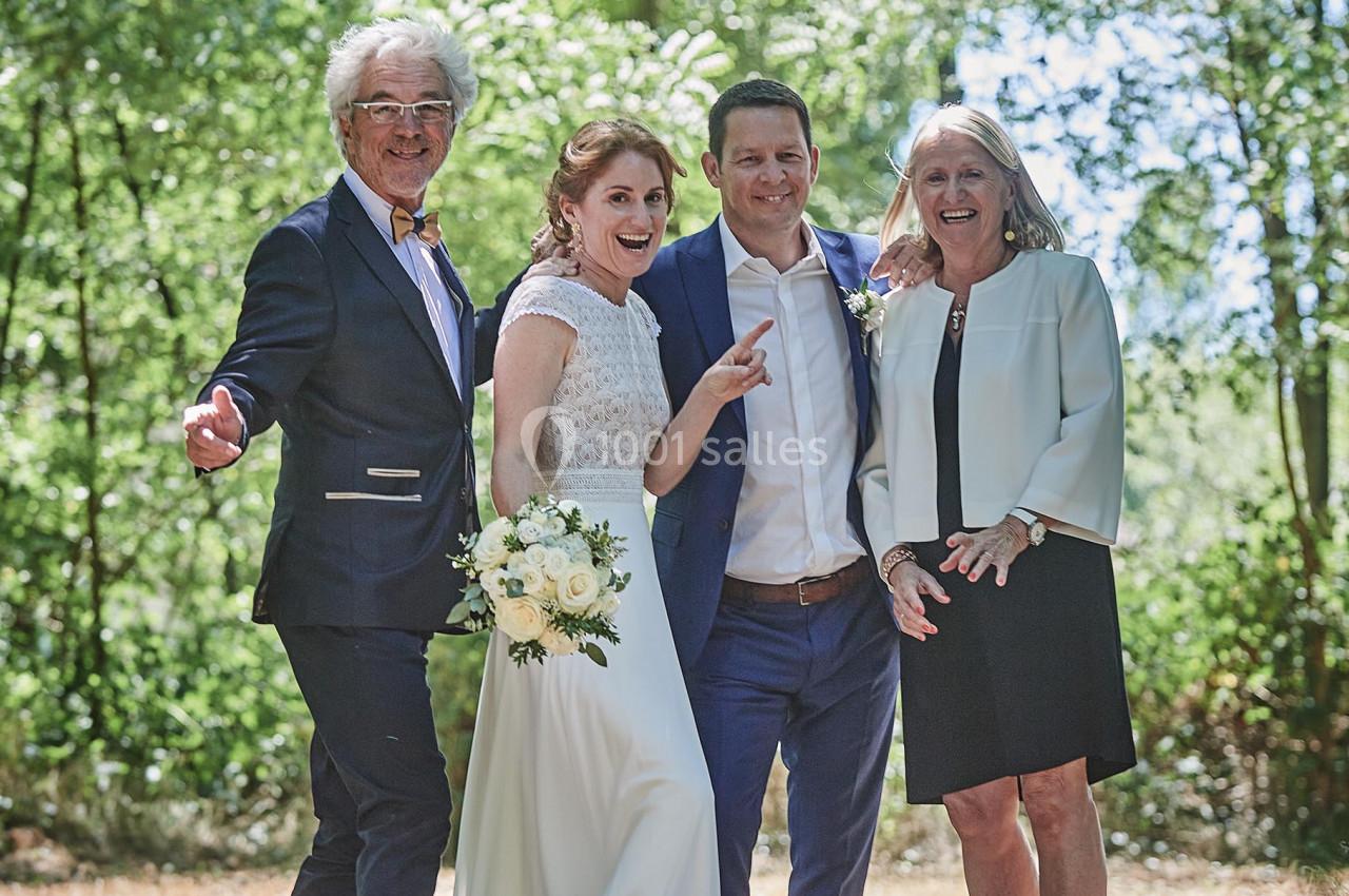 Un couple de mariés pose avec deux invités dans un cadre extérieur verdoyant.