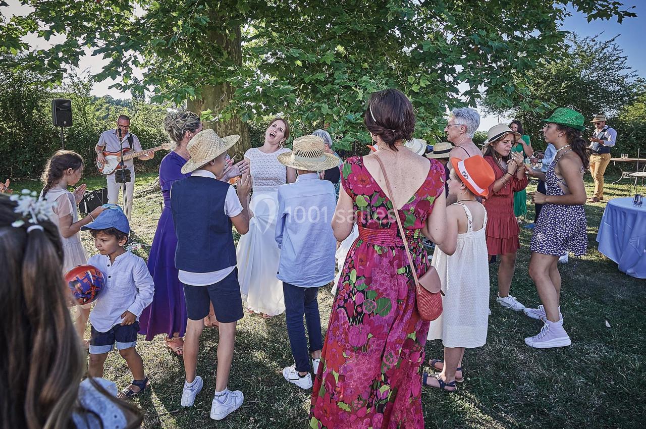 Groupe de personnes dansant et discutant en extérieur sous un arbre lors d'une fête en plein air.