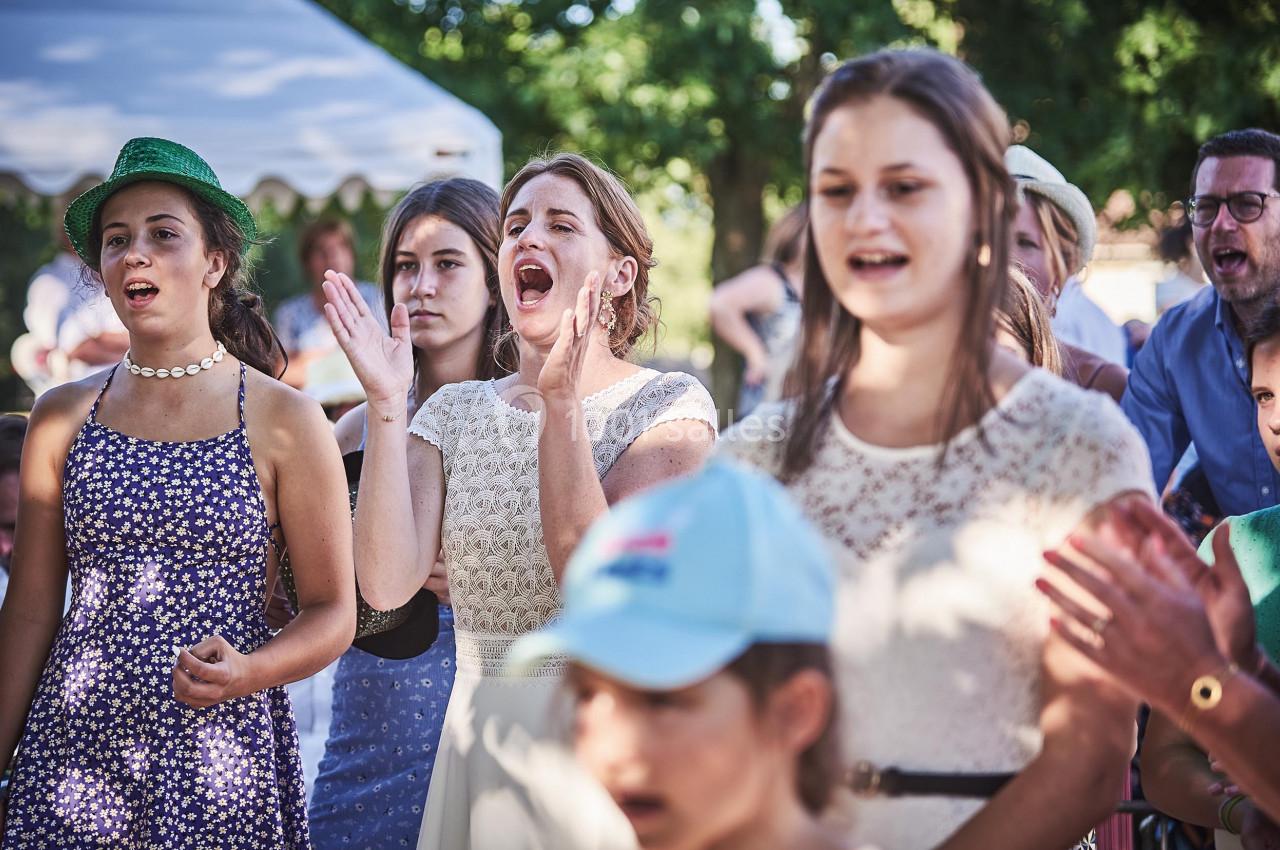 Des personnes applaudissent et chantent en plein air lors d'un événement festif sous un ciel dégagé.