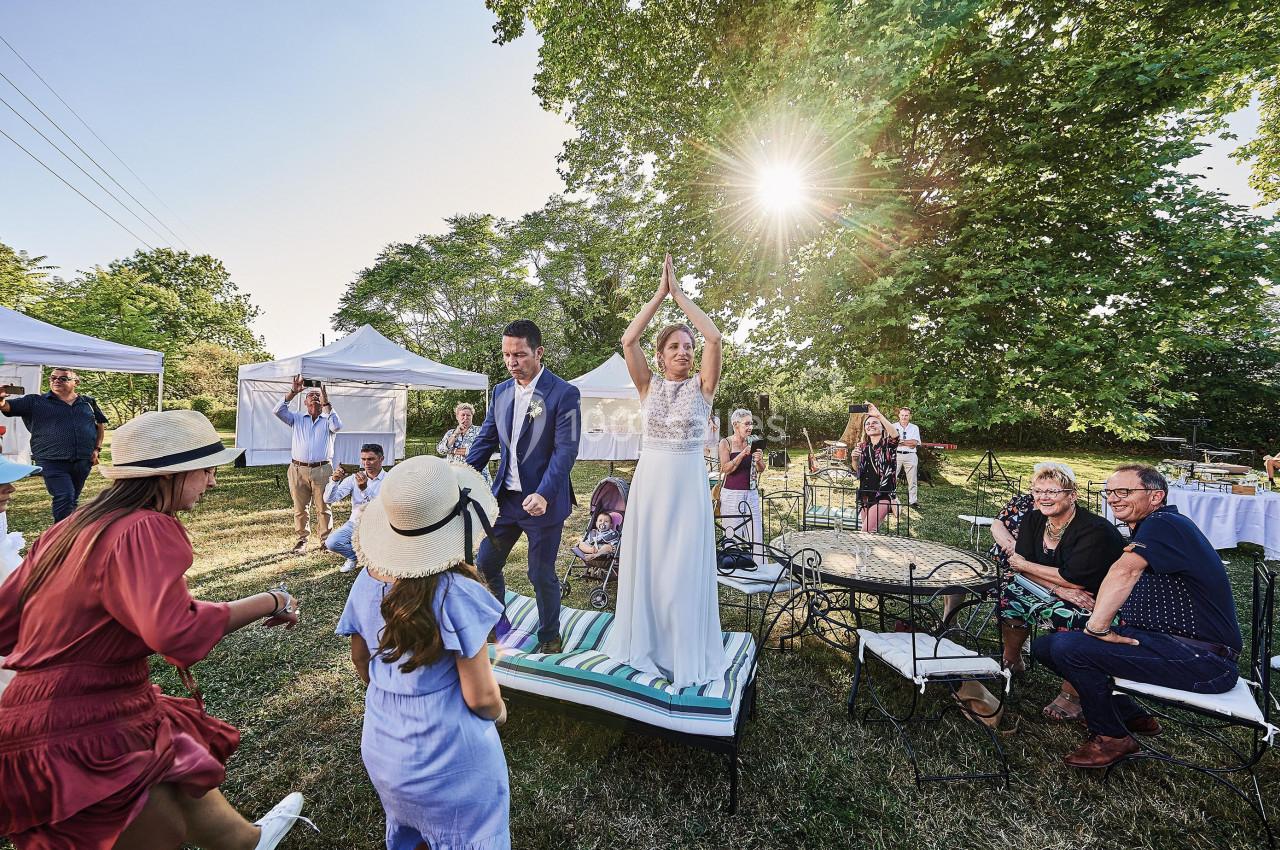 Un couple de mariés danse sur une estrade en extérieur, entouré d'invités assis ou debout sous un ciel ensoleillé.