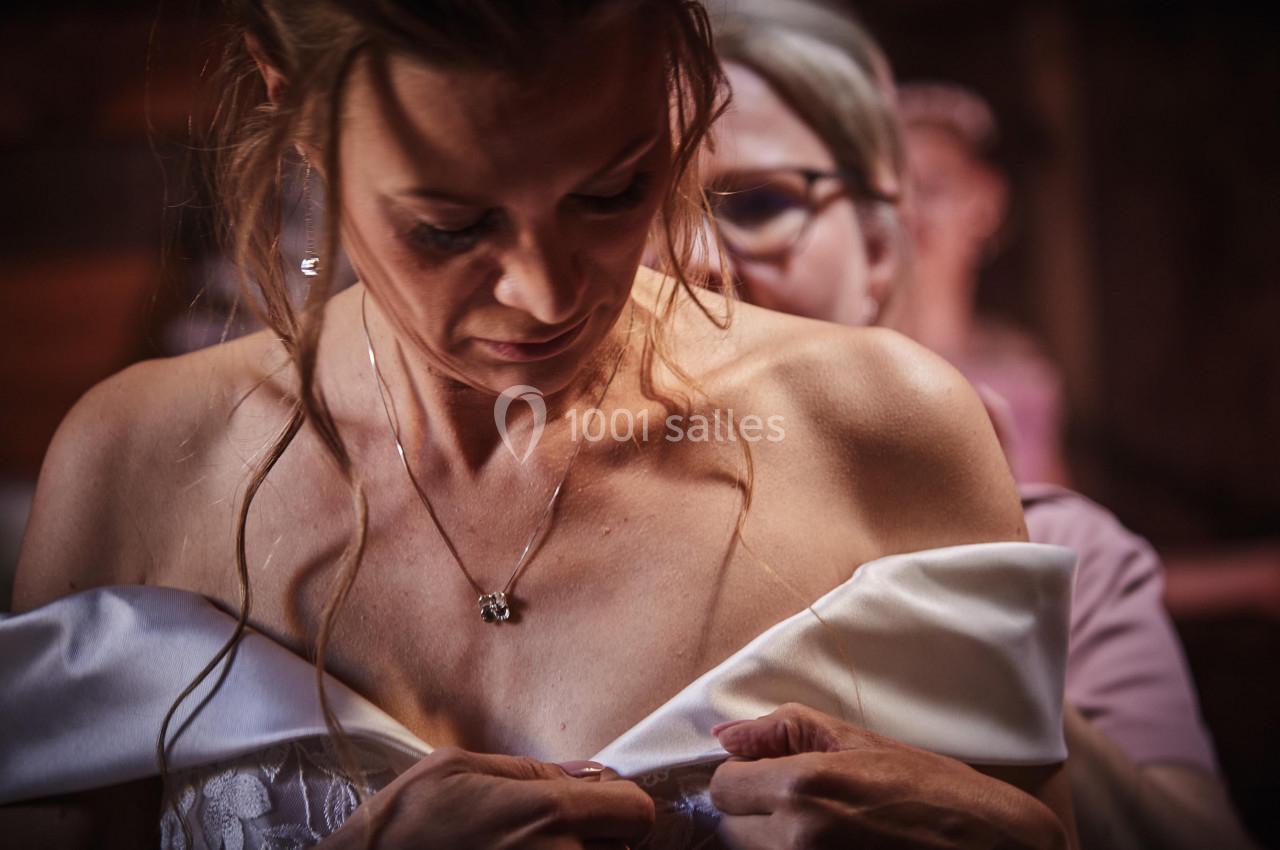 Une femme ajuste sa robe blanche épaules dénudées, aidée par une autre personne dans un environnement intérieur.