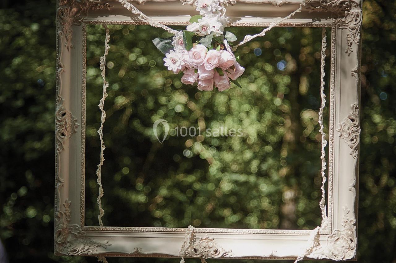 Cadre décoratif suspendu avec des fleurs roses au centre, placé dans un environnement naturel verdoyant.