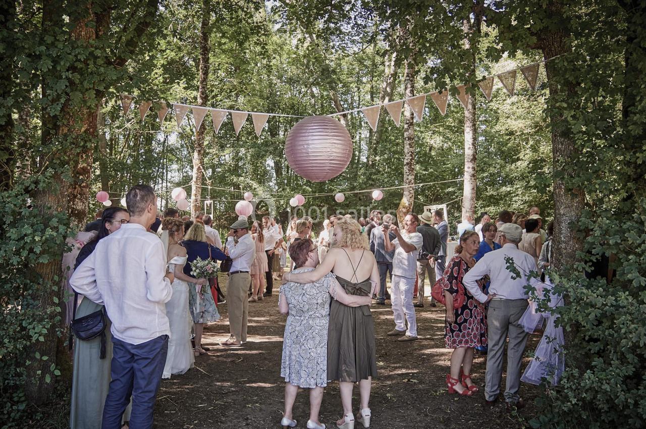 Groupe de personnes réunies dans une clairière décorée de guirlandes et lanternes pour un événement en plein air.