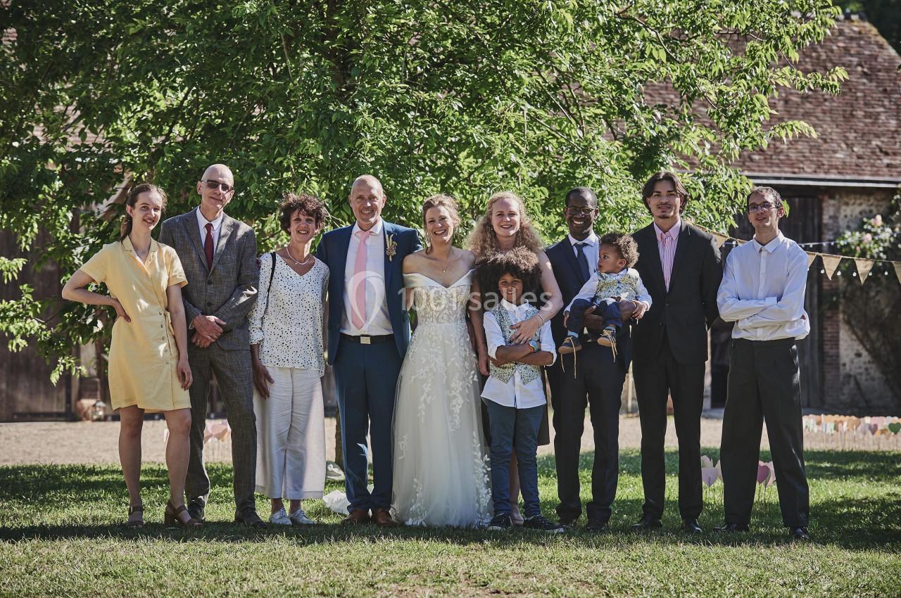 Un groupe de personnes posant ensemble en extérieur devant un arbre, dont un couple en tenue de mariage.