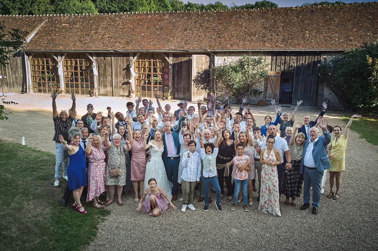 Un grand groupe de personnes pose joyeusement devant un bâtiment en bois dans un cadre extérieur.