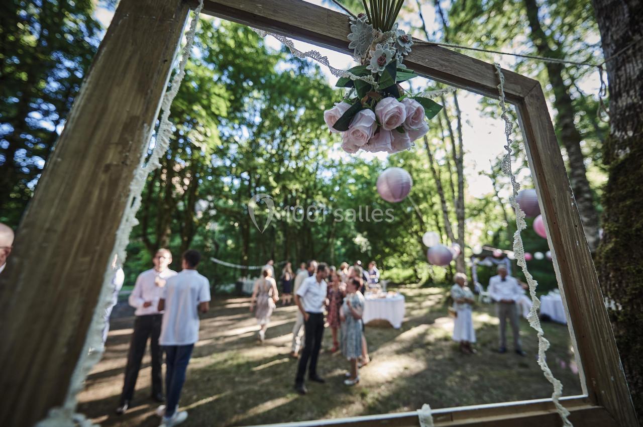 Cadre en bois décoré de fleurs roses, avec des invités discutant dans un jardin boisé en arrière-plan.