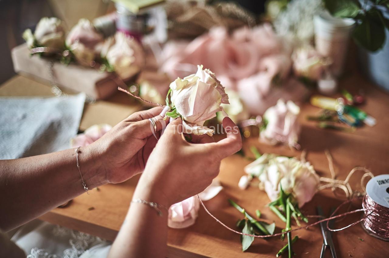 Personne assemblant des fleurs roses sur une table avec des outils et des matériaux de bricolage.