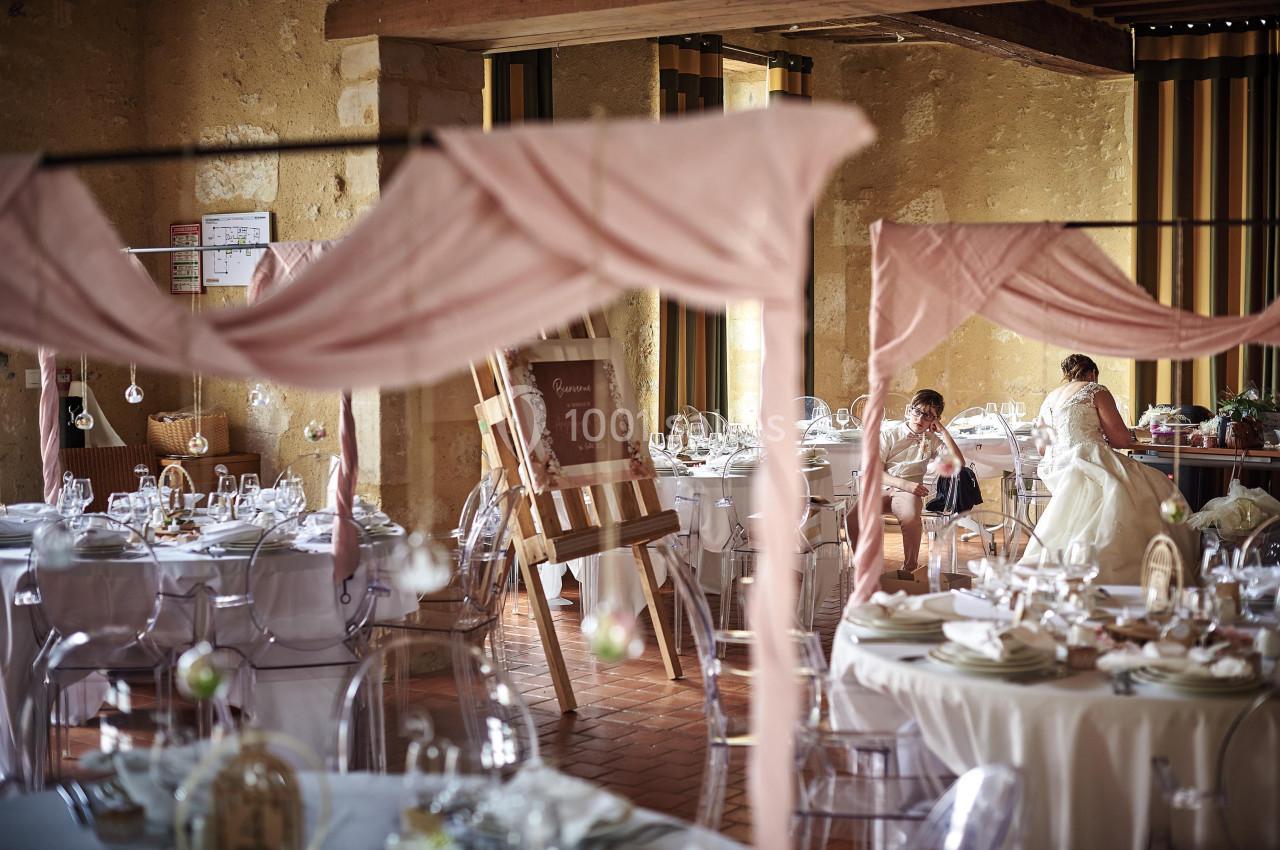 Salle de réception décorée avec des nappes roses, des tables dressées et des éléments suspendus, ambiance chaleureuse.