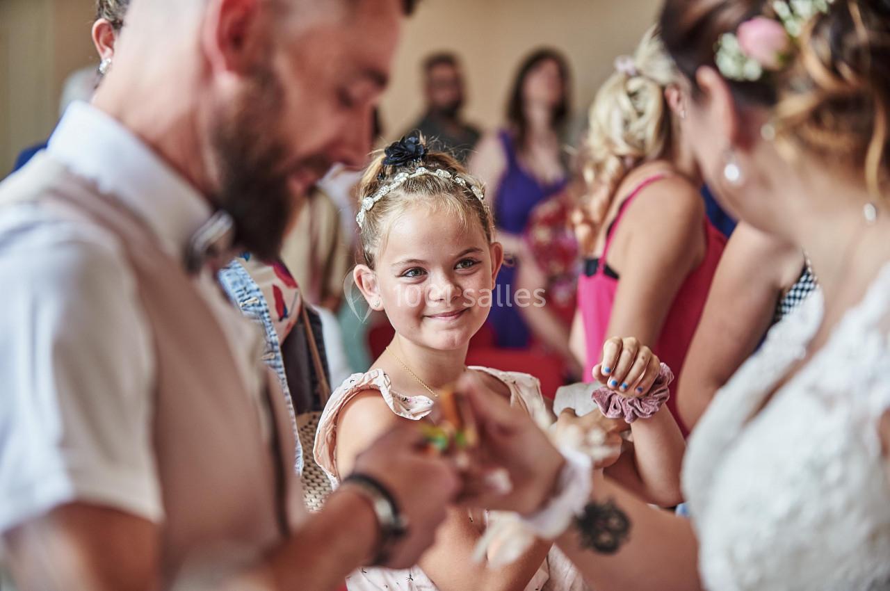 Une jeune fille sourit en regardant deux adultes échanger un objet lors d'un événement convivial.