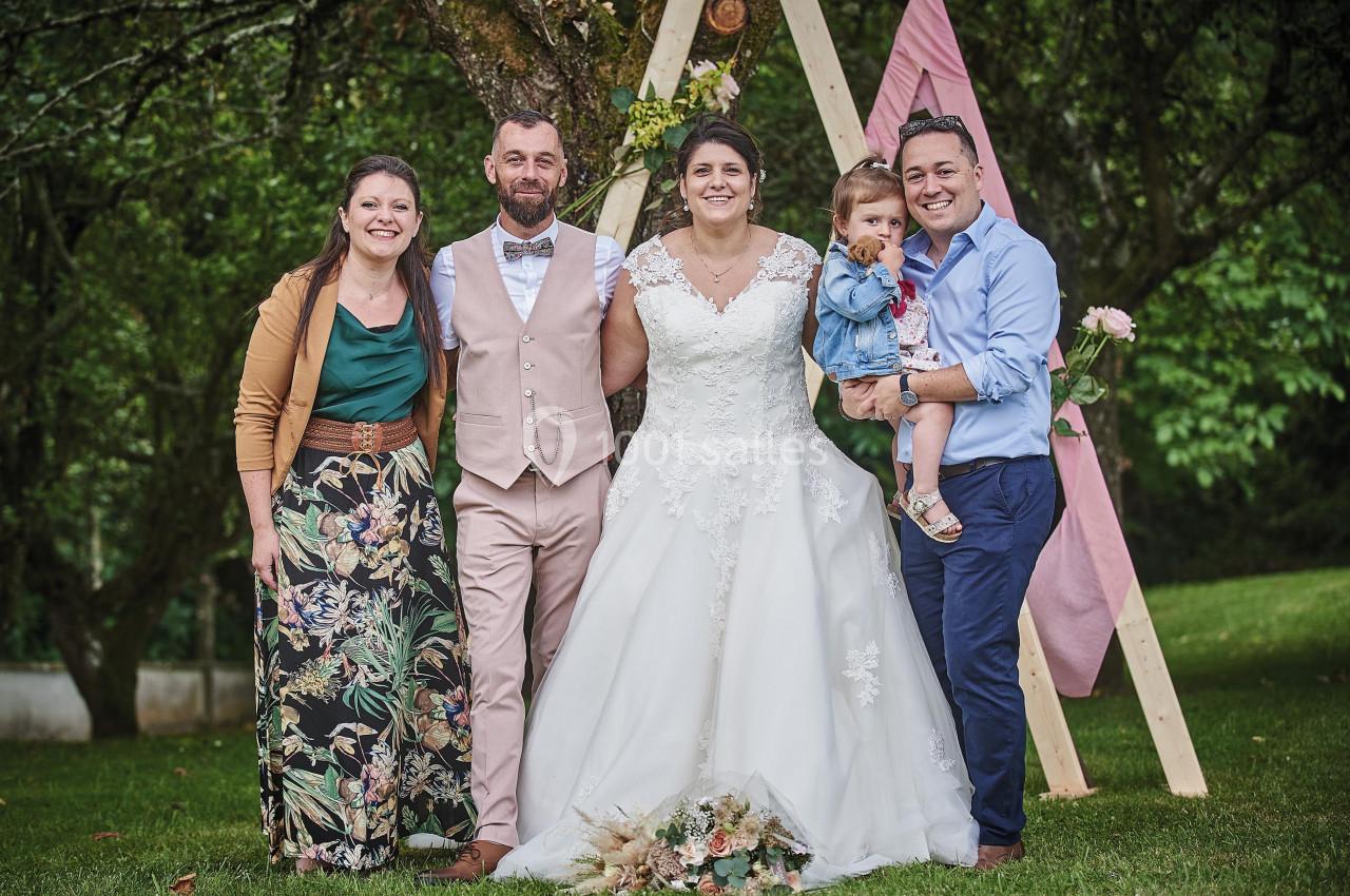 Un groupe de cinq personnes, dont un couple en tenue de mariage, posant devant un décor extérieur avec des arbres.