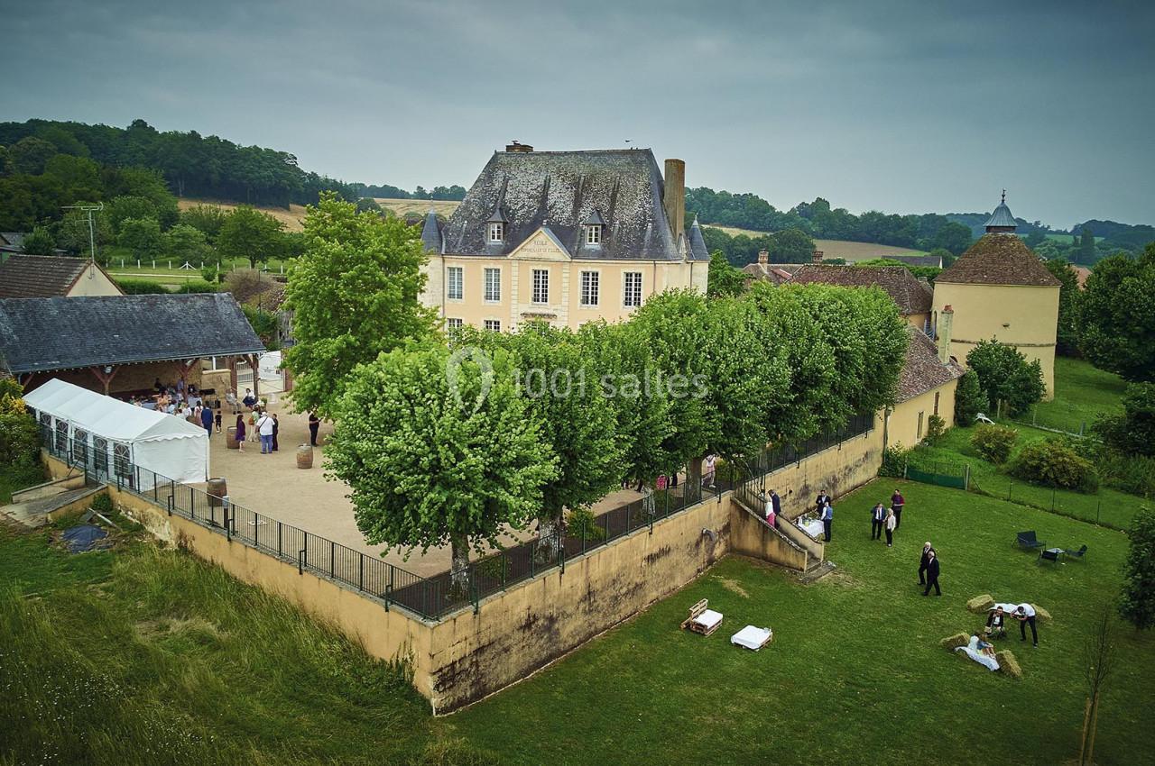 Vue aérienne d'une grande maison ancienne entourée d'arbres, avec des personnes dans la cour et le jardin.